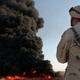 A giant black cloud of burning oil rises behind a U.S. Army soldier in August 2003.